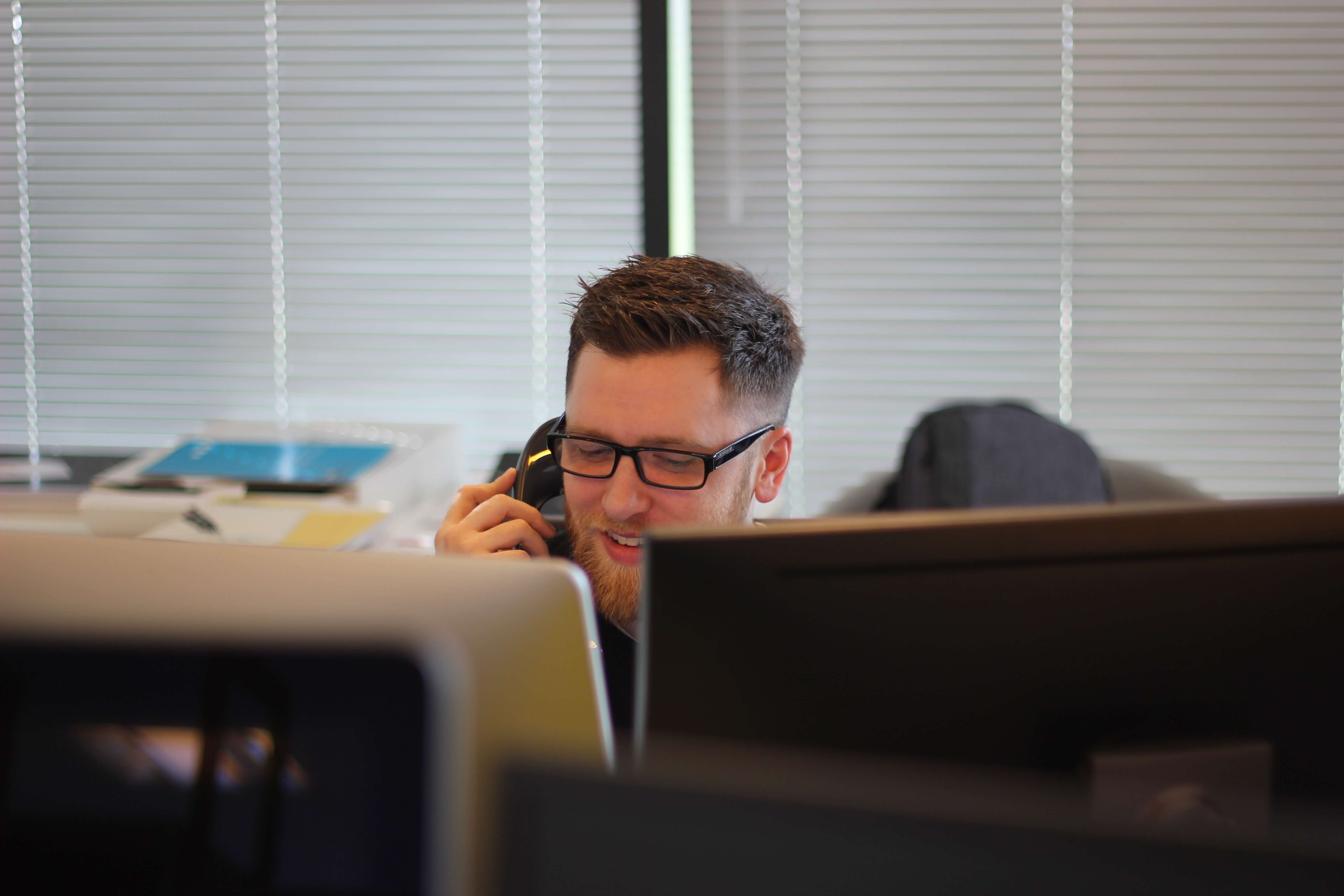 A smiling man wearing glasses with a phone received to his ear to help illustrate GB Electronics' after sales service.